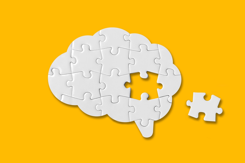 White jigsaw puzzle forming a brain shape on a yellow background with one piece missing, symbolizing problem solving or missing piece insight.