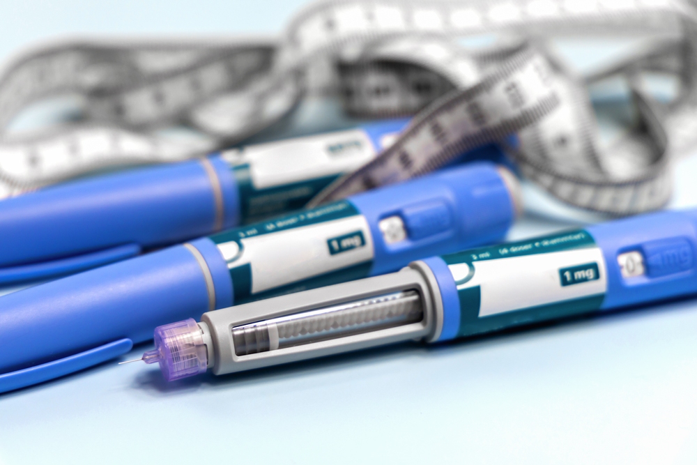 Blue insulin pens and a syringe on a light blue surface with a blurred measuring tape in the background, representing diabetes care supplies.