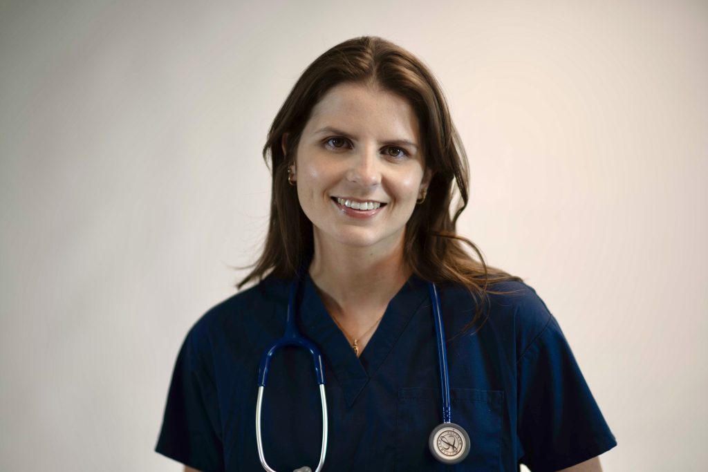 Female healthcare professional wearing navy scrubs with a stethoscope around her neck, smiling at the camera.