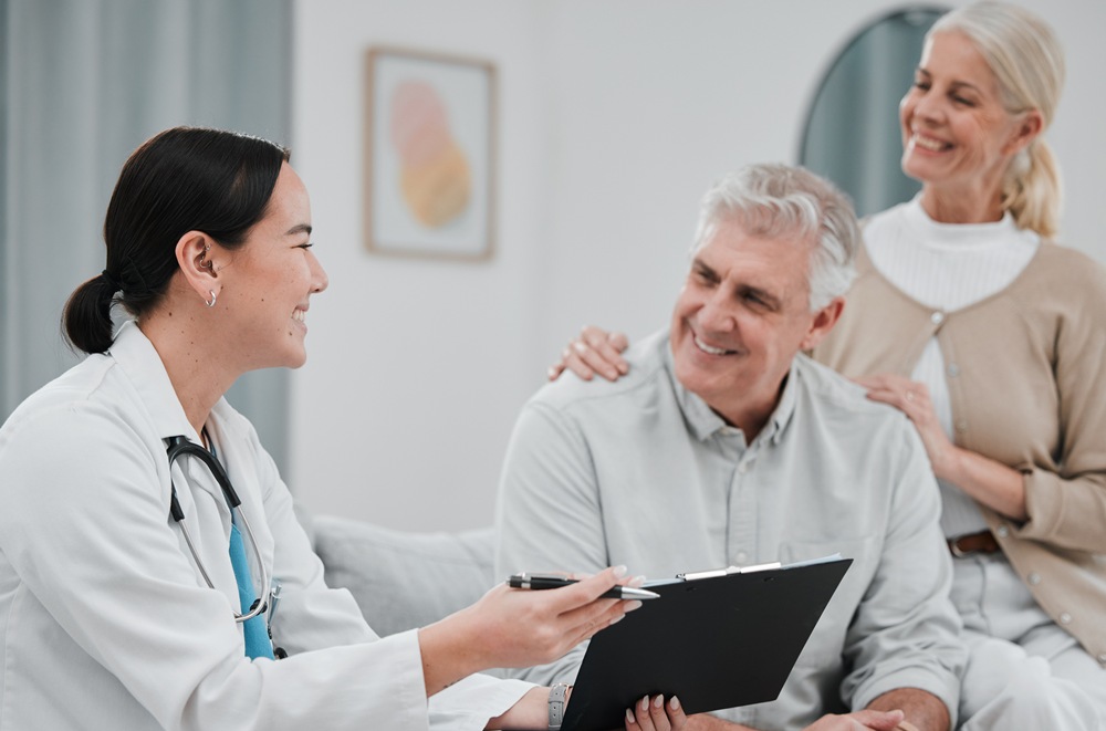 Doctor consults with a smiling older patient on a clipboard, while his partner stands behind with a supportive hand on his shoulder.